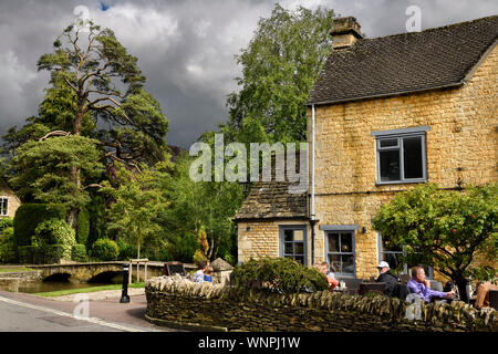 The Croft Pub auf der Terrasse in der Sonne mit Kiefern- und Fußgängerbrücke über den Fluss Windrush in Bourton-on-the-Water Gloucestershire England Stockfoto