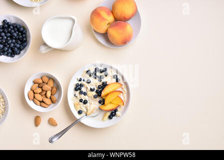 Gesunde Ernährung frühstück Konzept. Haferflocken Porridge mit Pfirsich Scheiben-, Mandel- und wilden Blaubeeren in Schüssel über Licht Stein mit Freien fo Stockfoto