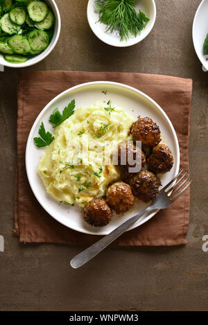 Die Koteletts aus Hackfleisch mit Kartoffelpüree auf weißen Platte über braunen Hintergrund. Ansicht von oben, flach Stockfoto