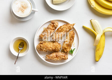 Frittierte Bananen auf die Platte über der weißen Stein Hintergrund. Leckere Dessert von Gebratene Bananen im asiatischen Stil. Ansicht von oben, flach Stockfoto