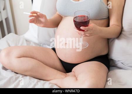 Schwangere Frau raucht eine Zigarette und trinkt Alkohol, Frau in der Schwangerschaft mit Tabak und Glas Wein Stockfoto