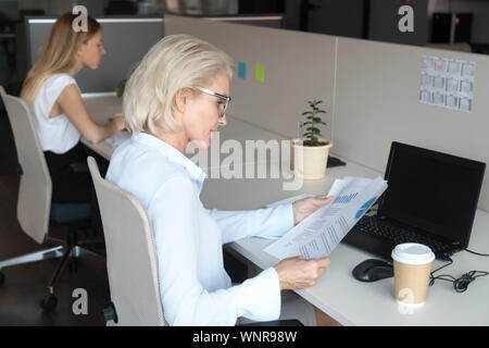 Konzentrierte sich Frau mittleren Alters lesen Finanzbericht an Shared Office Schreibtisch Stockfoto