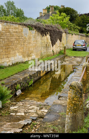 Wasser stehend in der alten Karre Waschen neben der Armenhäuser der Church Street Tetbury England mit gelben Cotswold stone Stockfoto