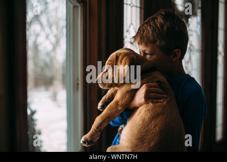 Junge holding Yellow lab Welpen aus Suchen Fenster bei Schnee. Stockfoto