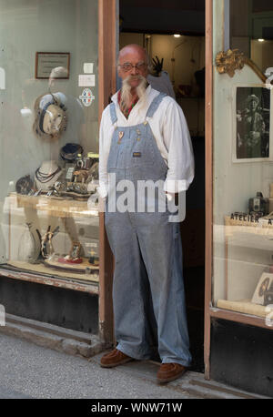 Alter Mann mit langem weißen Bart und Schnurrbart in Latzhosen wachen Store Front. Stockfoto