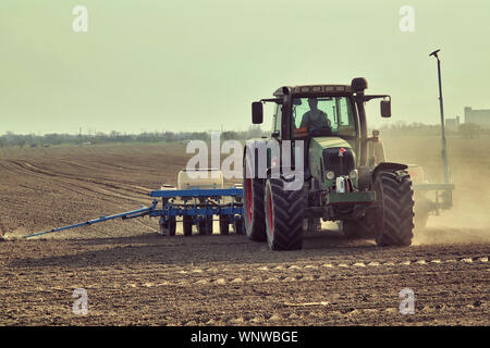 Den Traktor in einen Sonnenuntergang abschleppen Seeder und Sägen Korn wirbelnde Wolken von Staub Stockfoto