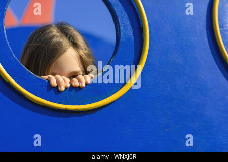 Junge Mädchen verstecken und spähen hinter dem Loch in der Wand von playhouse. Schüchterne Mädchen am Spielplatz. Angst kid Konzept. Stockfoto