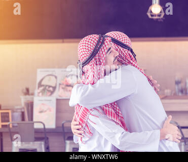 Zwei arabische Männer, die Freunde zusammen sind, umarmen und Lächeln, wenn Sie versehentlich an den Cafe & Restaurant am Morgen treffen Stockfoto