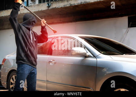 Auto Dieb Diebstahl Glas in ein Auto zu brechen. maskierte Gesicht Mann verbergen, Räuber in Schwarz holding Kurzschließer in Auto Schäden Glas Fenster des Autos gekleidet. Stockfoto