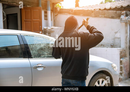 Auto Dieb Diebstahl Glas in ein Auto zu brechen. maskierte Gesicht Mann verbergen, Räuber in Schwarz holding Kurzschließer in Auto Schäden Glas Fenster des Autos gekleidet. Stockfoto