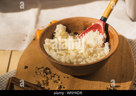 Reisbrei in einer Töpferei mit Butter. Im rustikalen Stil mit einem Holzlöffel. Milch Brei auf einem Holztisch. Stockfoto