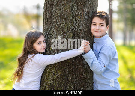 Junges Mädchen und junge spielt um den Baum im Park. Romantische Kinder im Park. Freund und Freundin der Baum im Park umfassen. Stockfoto