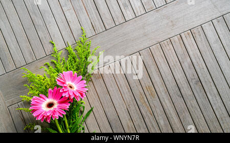 Rosa Gerbera Daisies mit grünen Pflanzen auf Holztisch. kopieren. Stockfoto