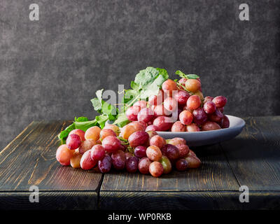 Frischen Weintrauben. Trauben von verschiedenen Sorten in einer Platte auf einem alten Holztisch und dunklen Hintergrund. Soft Focus Stockfoto