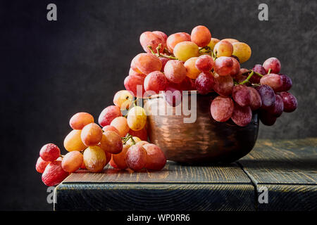 Frischen Weintrauben. Trauben von verschiedenen Sorten in einer Platte auf einem alten Holztisch und dunklen Hintergrund. Soft Focus Stockfoto