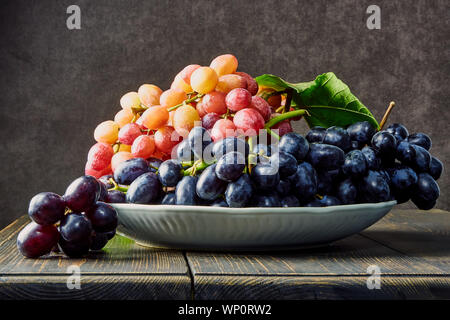 Frischen Weintrauben. Trauben von verschiedenen Sorten in einer Platte auf einem alten Holztisch und dunklen Hintergrund. Soft Focus Stockfoto