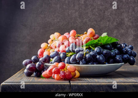 Frischen Weintrauben. Trauben von verschiedenen Sorten in einer Platte auf einem alten Holztisch und dunklen Hintergrund. Soft Focus Stockfoto