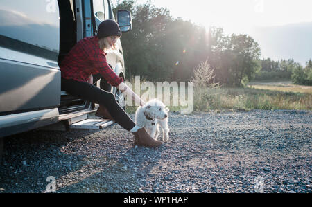 Frau sitzt auf einem Wohnmobil streicheln Ihren Hund beim Camping Stockfoto