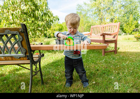 Toddler boy sieht frustriert während der Messung Holzbrett im Freien Stockfoto