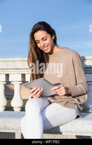 Lachende Frau mit der Tablette, während auf einer Bank sitzt Stockfoto