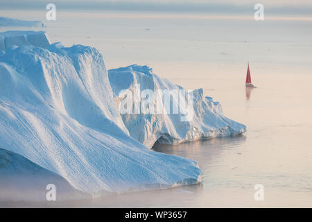 Kleine rote Segelboot Kreuzfahrt unter schwimmende Eisberge in der Diskobucht Gletscher mitternachtssonne Saison von polaren Sommer. Ilulissat, Grönland. Unesco Stockfoto