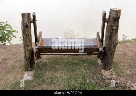 Schaukeln Sitzbank am Ufer eines Teiches. Leere Holz- Schwingen an der Küste. Stockfoto