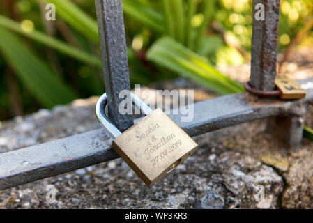Messing Vorhängeschloss oder Liebe Sperren mit den Namen von ein paar an den schmiedeeisernen Bar von einem Zaun in der Nähe zu sehen, befestigt Stockfoto