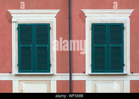 Windows mit geschlossenen grünen Fensterläden aus Holz und weißen umgibt, in einem tiefen Rot Rosa Wand in einem symmetrischen full frame Architektur Hintergrund Stockfoto