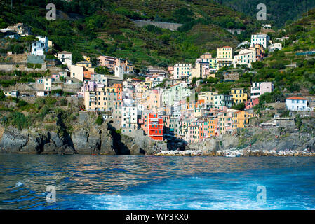 Blick auf die farbenfrohe Architektur der populären Riomaggiore, Cinque Terre, Ligurien, Italien vom Meer mit einem Kreuzfahrtschiff oder Fähre in der foregro Stockfoto