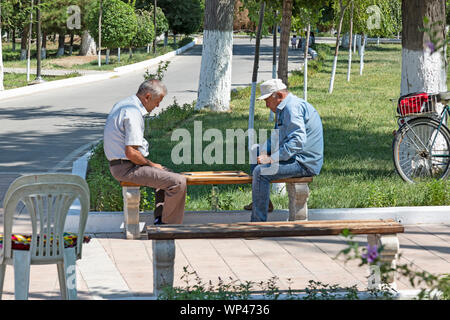 Zwei ältere Herren sitzen auf einer Parkbank, in einem Park in Buchara, Usbekistan, spielen Backgammon. Stockfoto