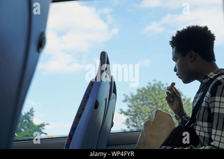 Ein junger Mann essen ein gebratenes Huhn auf einem London Bus Stockfoto