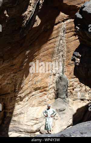 Mann in traditioneller Kleidung steht in der Nähe der Felsformation in der Nähe von Balad Sayt, Oman Stockfoto