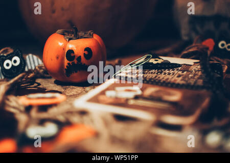 Halloween kleine Kürbis mit bemalten Gesichtern auf einem Holzboden, daneben ist ein Notebook mit Fledermäusen, Handarbeit die Vorbereitung für den Urlaub. Stockfoto