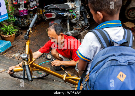 Ein junger asiatischer Boy ist ein Mann test Reifendruck mit einem Manometer an einen reparierten Reifens an eine Stadt Straße in Phnom Penh, Kambodscha. Stockfoto