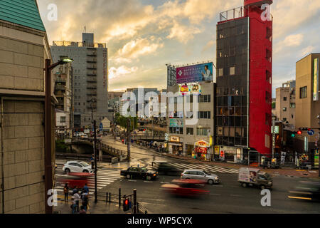 Fukuoka, Japan - 10. Juli 2019 - Autos und Fußgänger reisen auf und entlang einer Straße von Fukuoka, Japan an einem regnerischen Abend des 10. Juli, 2019 in Fukuoka, Ja Stockfoto