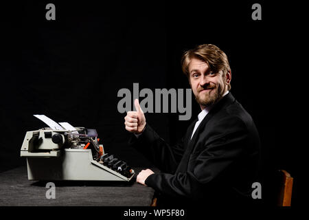 Schriftsteller, ein Mann in einem schwarzen Mantel Tippen auf der Schreibmaschine auf schwarzem Hintergrund Stockfoto