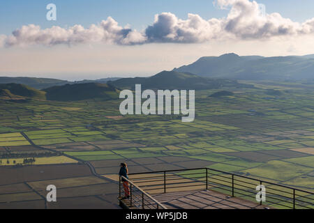 Eine junge Frau genießen und dabei den Blick auf die Felder von der Aussichtsplattform der Miradouro Da Serra do Cume auf der Insel Terceira an einem schönen Sonnen Stockfoto