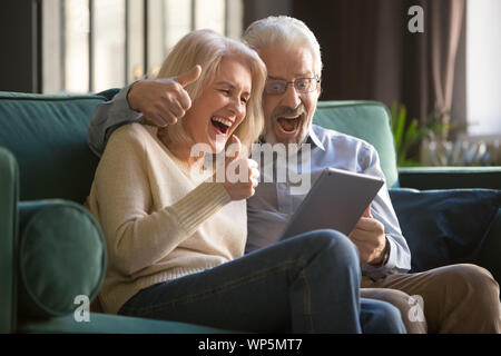Grauhaarige glückliches junges Paar feiern gemeinsam online gewinnen. Stockfoto