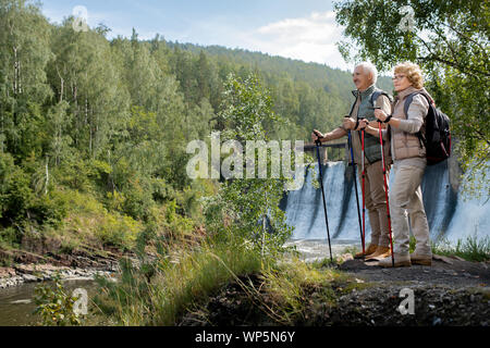 Zwei glückliche reife Backpackers in Activewear stehend durch Wald Fluss Stockfoto