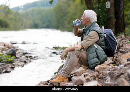 Müde reife Backpacker Trinkwasser aus Kunststoff Flasche am Flussufer Stockfoto