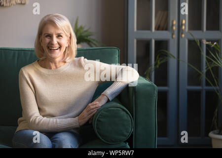 Gerne ältere Frau von 60 s auf der Couch zu Hause sitzen Stockfoto