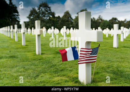 Selektive Lupenansicht des Kreuzes Grundsteine im Amerikanischen Friedhof in Omaha Beach in der Normandie mit französischen und US-Flaggen Stockfoto