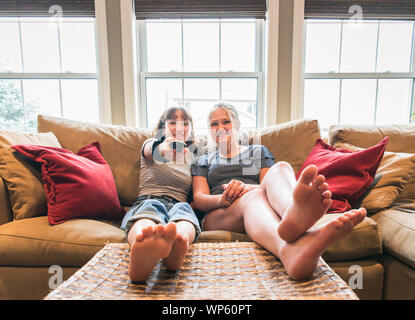Zwei Mädchen sitzen auf einer Couch mit Füßen bis Fernsehen. Stockfoto