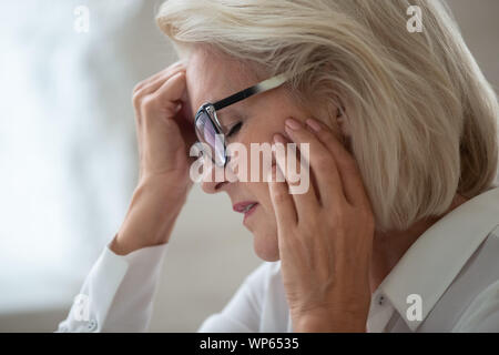 Betonte gealterte Frau in Gläsern leiden unter Kopfschmerzen. Stockfoto