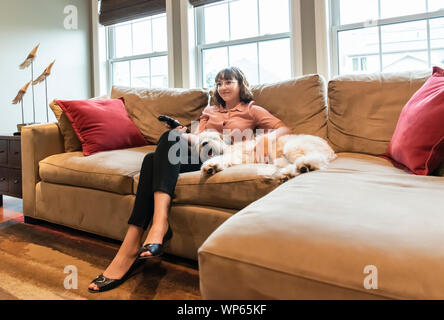 Junge Frau in Geschäftskleidung sitzen auf der Couch mit Hund TV schauen. Stockfoto