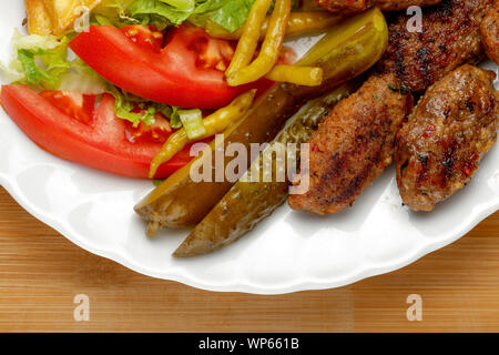 Eine Platte mit Frikadellen mit Pommes, Gurken, Gemüse auf dem hölzernen Tisch Stockfoto