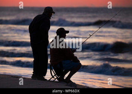 Mit einem Freund über seine Schulter, ein Fischer sitzt und wartet auf einen Biss im Morgengrauen auf Portsmouth Insel entlang von North Carolina Outer Banks. Stockfoto