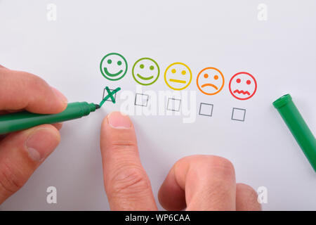 Hand Kennzeichnung eine positive Zufriedenheit mit fünf farbigen Emoticons auf weißem Papier vertreten. Horizontale Komposition. Ansicht von oben. Stockfoto