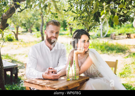 Attraktive Paar Jungvermählten, glücklichen und freudigen Moment. Braut und Bräutigam am Tisch für Zwei im Wald, sitzen. Konzept romantisches Date. Hochzeit paar Stockfoto