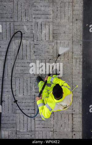Blick von oben auf ein Arbeiter die Straße Gehweg mit Hochdruck Wasserstrahl reinigen. Öffentliche Wartungskonzept Stockfoto
